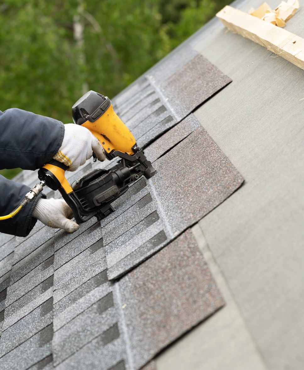 man nail gunning shingles to roof