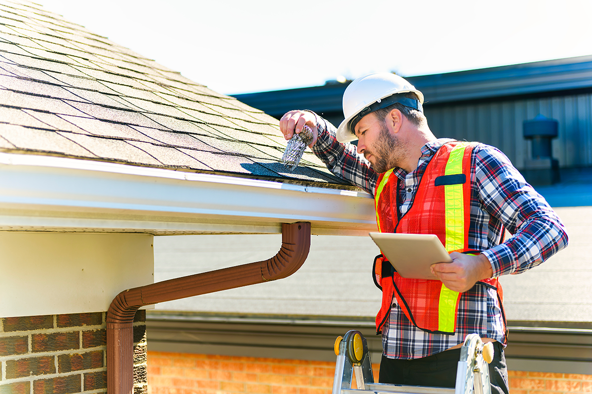 man wearing hard hat standing on steps inspecting house roof