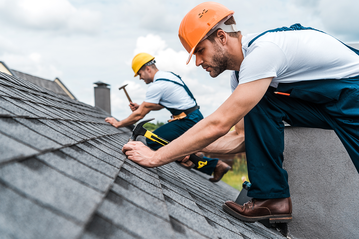 selective focus of handsome handyman repairing roof with coworker
